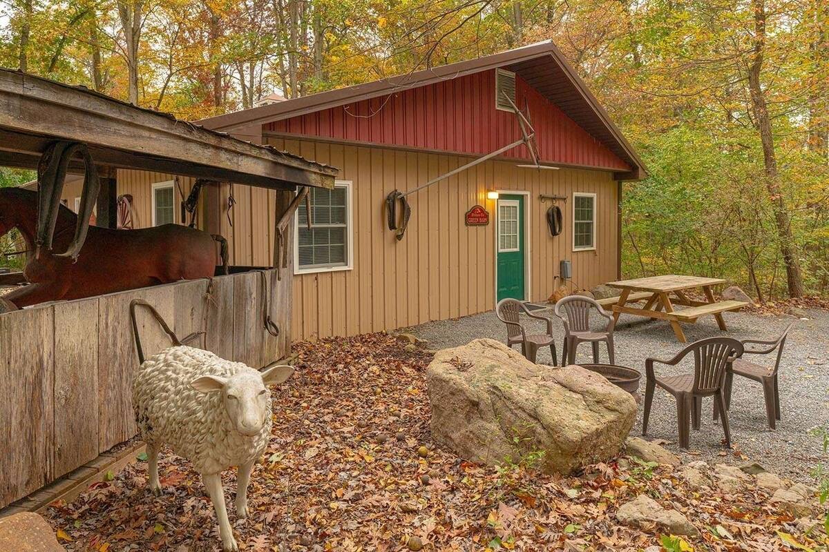 A rustic cabin with a stable, a picnic table, and a sheep sculpture.