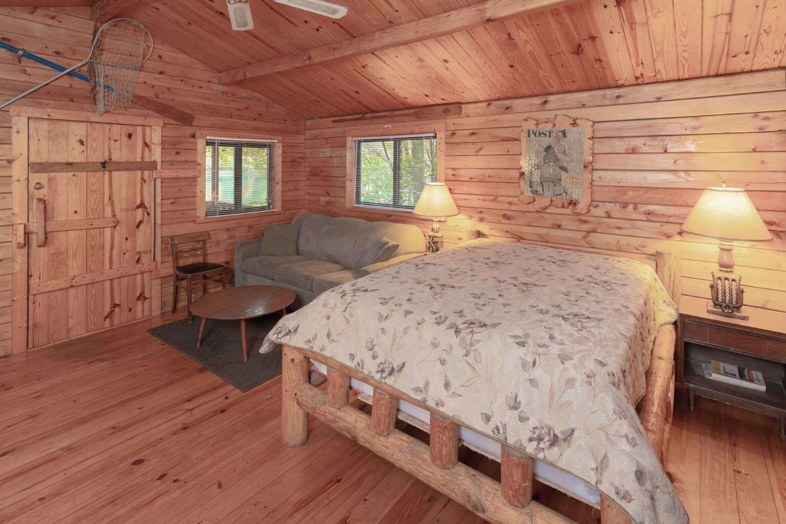 Quarto de cabana de madeira com uma cama, um sofá, uma mesinha e duas luminárias.