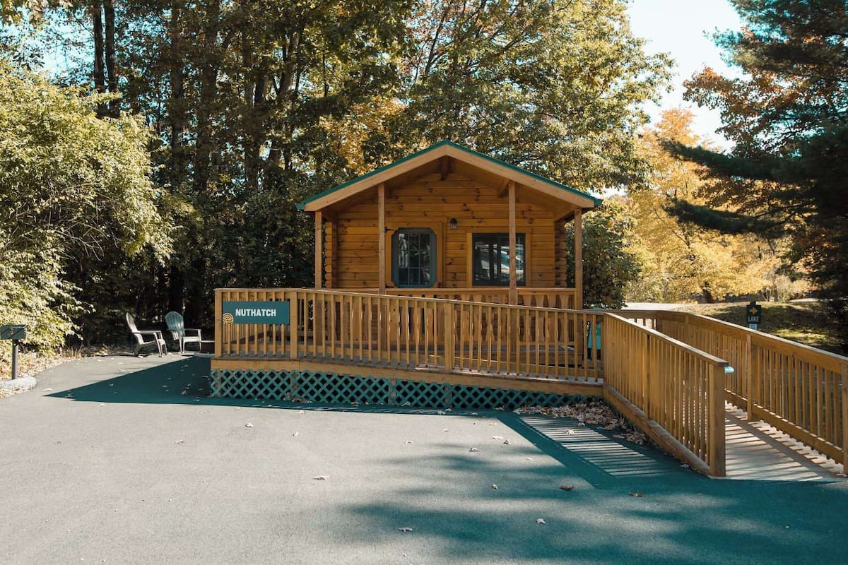 A wooden cabin with a porch, a sign reading 'NUTHATCH,' and a sign indicating 'LAKE' nearby.