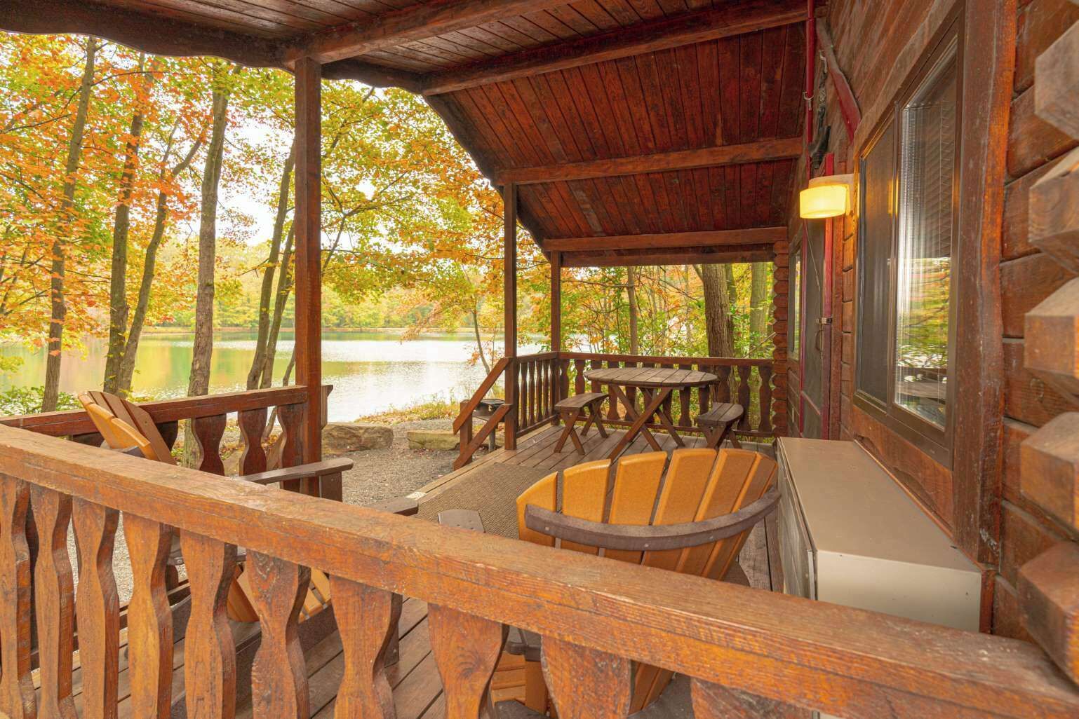 A wooden deck with a table and chairs, a fire pit, and a view of a lake surrounded by trees.
