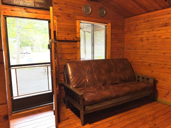 A wooden cabin interior with a leather sofa, a door with a screen, and two windows with blinds. - Sun Retreats Lancaster County (Narvon)