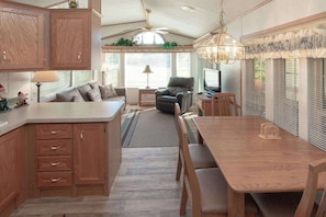 Una cocina con armarios de madera, una mesa de comedor con sillas, un sofá, un televisor y un ventilador de techo.