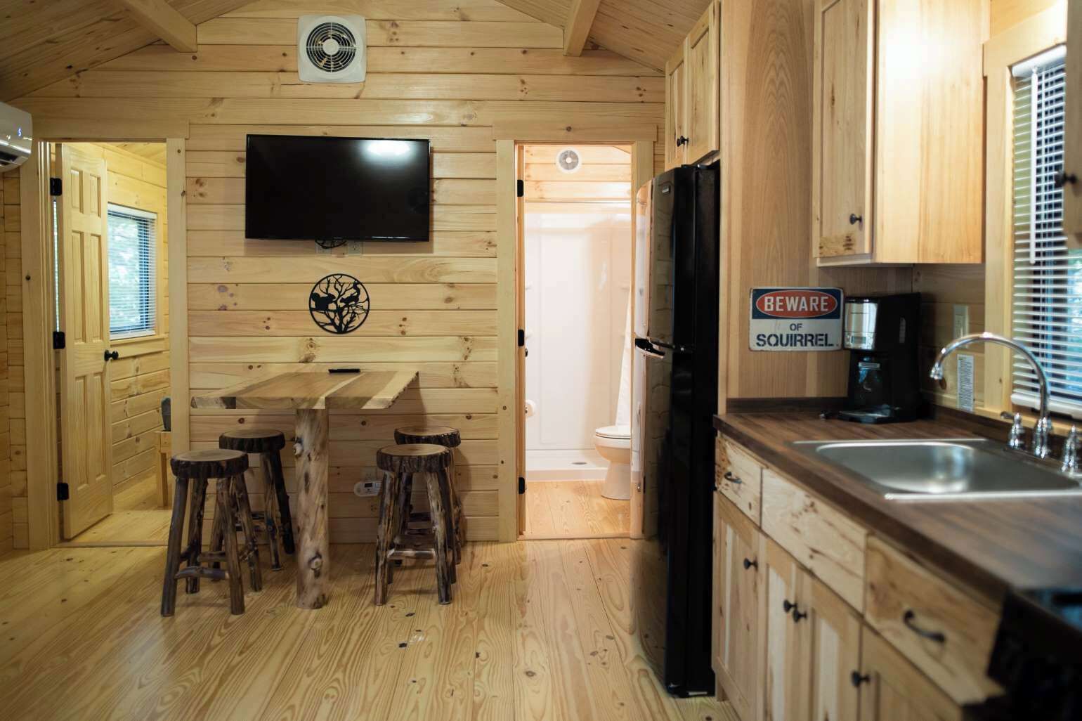 A wooden cabin interior with a kitchen, bar area, and a mounted television.