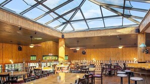 A restaurant with a high ceiling and a glass roof, wooden walls, and multiple dining tables and chairs.