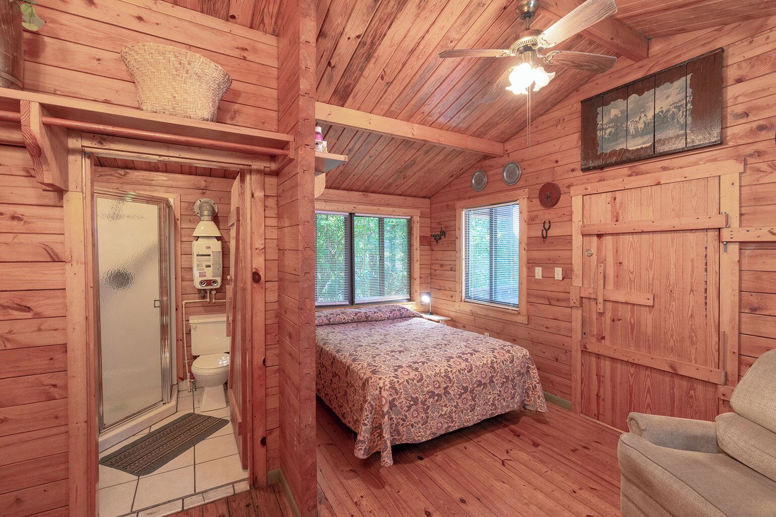Eine Holzhütte mit einem Bett, einem Badezimmer und einem Deckenventilator.
