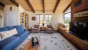 Uma sala de estar com um sofá azul, duas poltronas, uma mesa de centro, uma lareira, uma televisão e uma estante de livros.