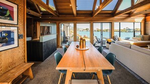 Een ruime eethoek met een lange houten tafel, omringd door stoelen, en uitzicht op het water.