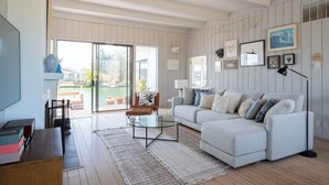 A spacious living room with a large sofa, a glass coffee table, and a view of a garden through a sliding glass door.