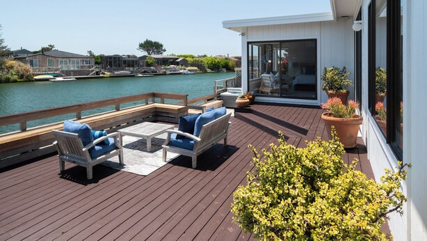 A deck with outdoor furniture, a view of the water, and a building with large windows.