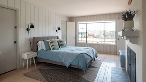 A bedroom with a bed, bedside tables, a window, and a view of the outside.