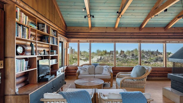 Interior acogedor de una cabaña con paredes y techos de madera, una amplia estantería, asientos cómodos y vistas al exterior.