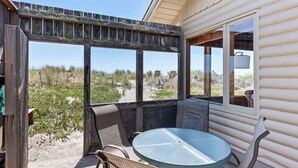Un espacio al aire libre cubierto con una mesa redonda y sillas, con vistas a un paisaje arenoso y vegetación escasa.