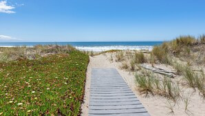 A wooden boardwalk leading to the beach, surrounded by grassy dunes and vegetation.