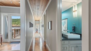 A hallway with wooden floors, framed artwork on the walls, and a view of a balcony.