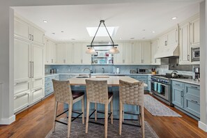 A modern kitchen with white cabinets, a central island with chairs, a skylight, and built-in appliances. - Spectacular Oceanfront Luxury Home in Seadrift (Stinson Beach)