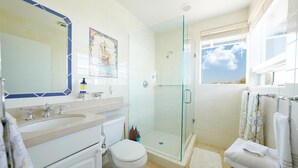 Une salle de bain moderne avec une douche à parois de verre, un grand miroir et une fenêtre donnant sur le ciel.