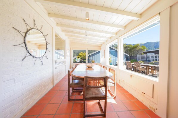 A sunlit dining area with a long table and chairs, a decorative mirror on the wall, and a view of the outdoors. - Cozy Oceanfront Getaway in Seadrift (Stinson Beach)