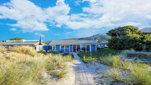 Une maison située sur la côte, avec un chemin pavé menant à l’entrée, entourée de dunes et de végétation.