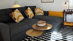 En moderne stue med en grå sofa, mønstrede puder, et lille træbord og en gulv med striber i sort og hvid.