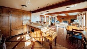 Une cuisine spacieuse avec des meubles en bois, un grand îlot central et un coin repas doté d’un sol en briques.