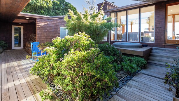 A modern house with a wooden deck, a hot tub, and a large glass window.