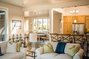 A spacious living room with a large sofa, a dining area with wooden chairs, and a kitchen with wooden cabinets and stainless steel appliances.