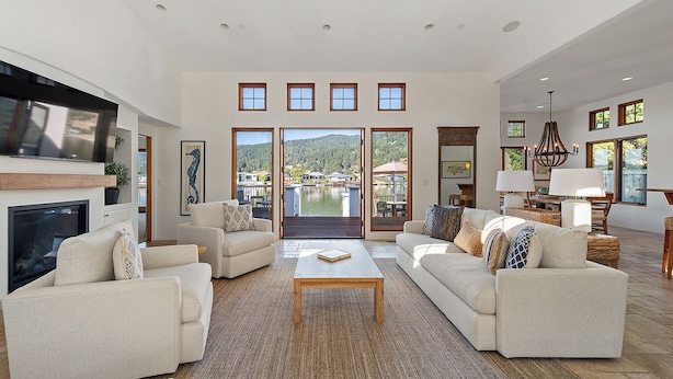 A spacious living room with a large TV, comfortable seating, a fireplace, and a view of a lake through large doors. - Light and Breezy Seadrift Lagoon Home w/ Hot Tub (Stinson Beach)