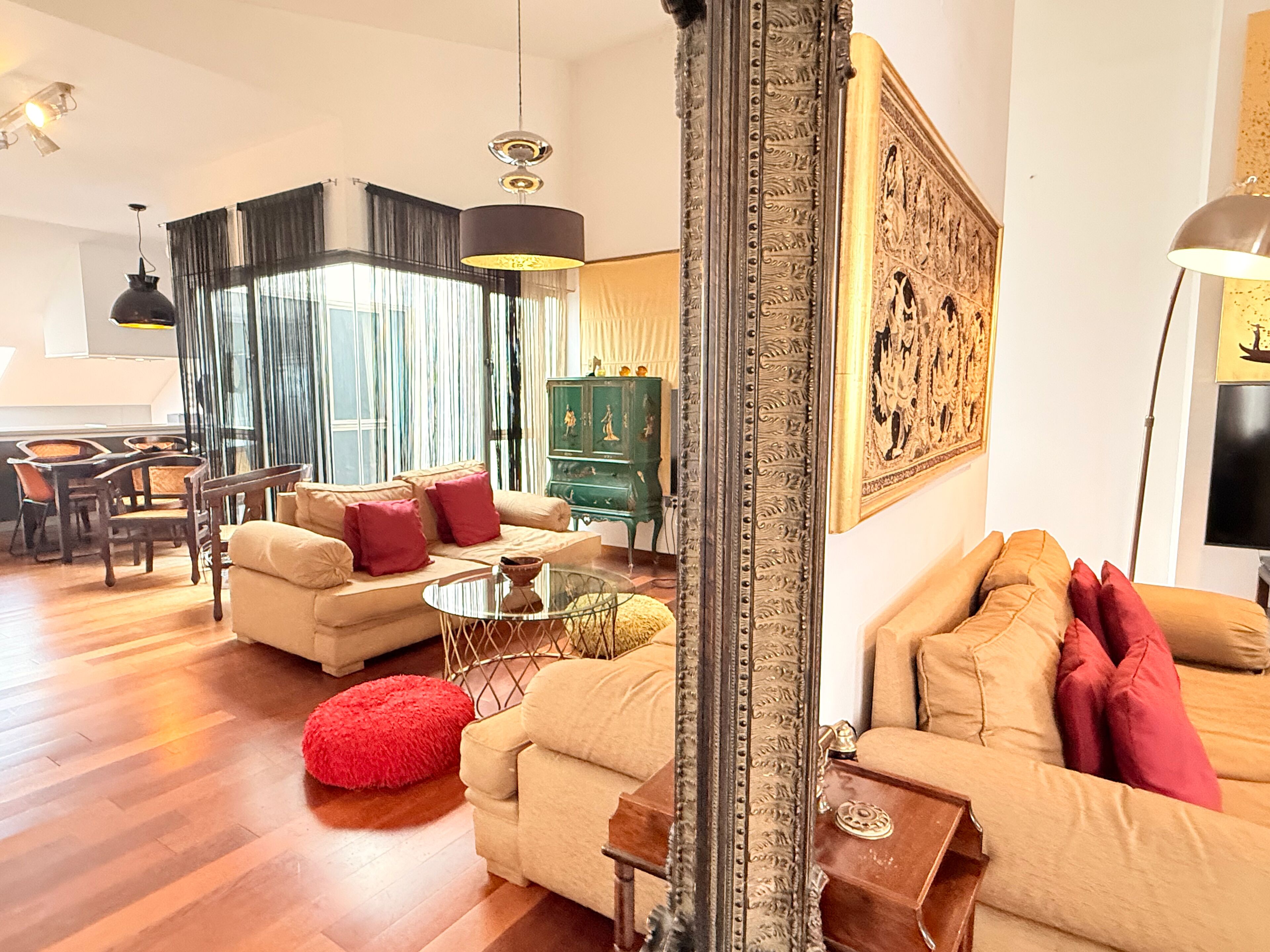 A spacious living room with a sofa set, a red ottoman, a green cabinet, and a large framed artwork on the wall.