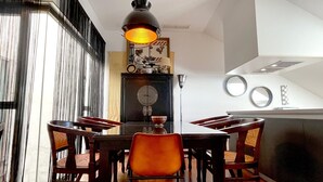 Uma área de refeições com uma mesa redonda, cadeiras de madeira e uma luminária pendente.