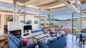 Amplia sala de estar con chimenea, asientos y un gran ventanal con vista al agua.