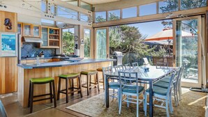 Una cocina moderna con una isla central, taburetes de bar y una zona de comedor con mesa de vidrio y sillas.