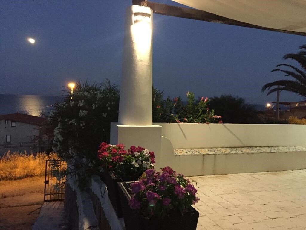 En udendørs patio med en hvid søjle, krukker med planter og udsigt til havet.