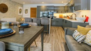 Une cuisine moderne avec des meubles gris, un îlot central et un coin repas comprenant une table en bois et des chaises grises.