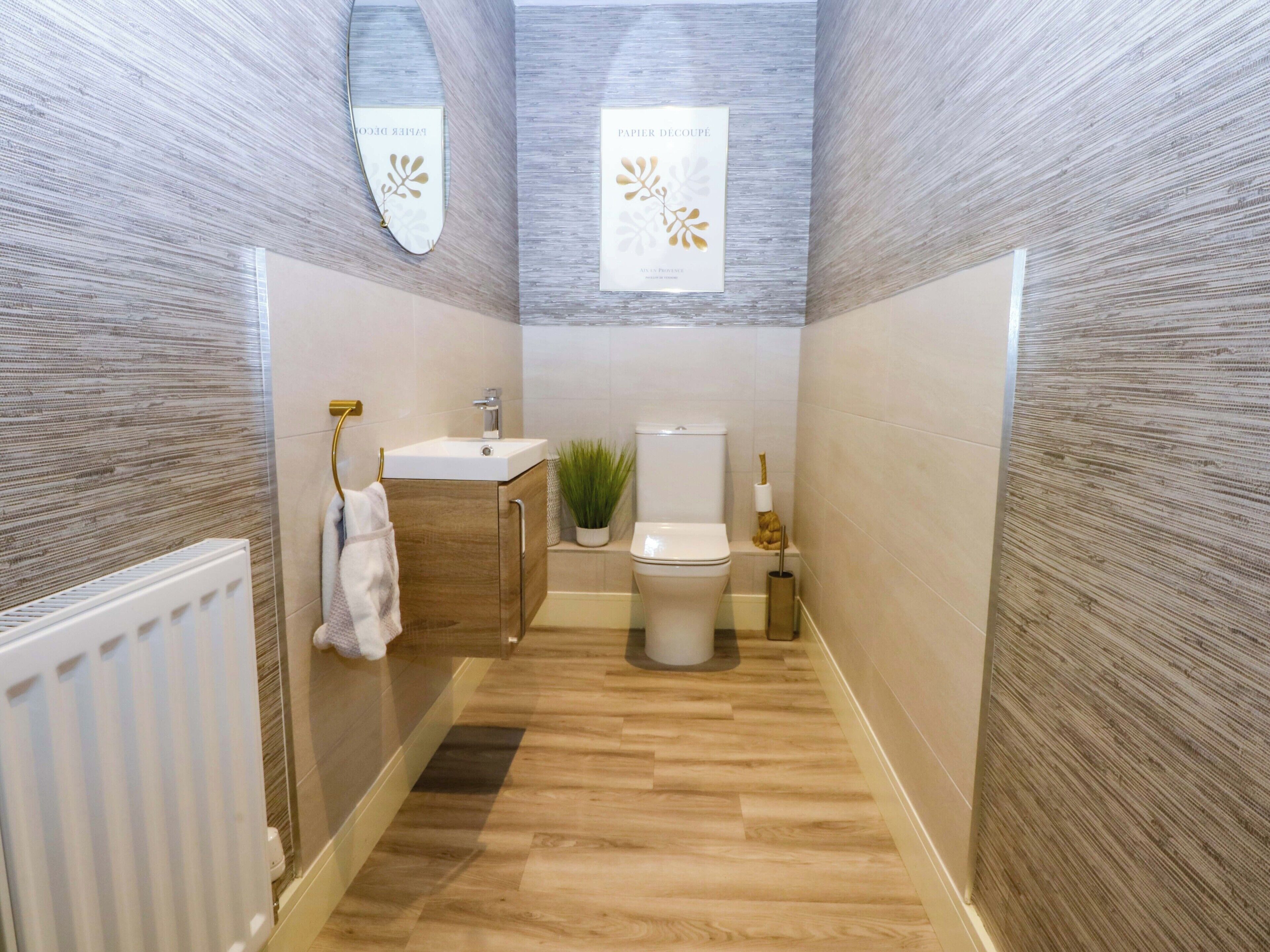 A narrow bathroom with a wooden floor, a white sink, a toilet, and a towel rack.