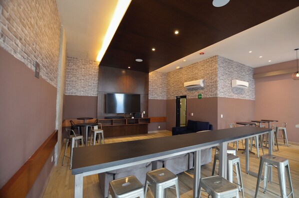 Una zona de bar moderna con una barra larga, taburetes y un televisor.