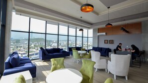 A modern lounge with large windows, blue sofas, green chairs, and a bar area. - Amo Living (Monterrey)