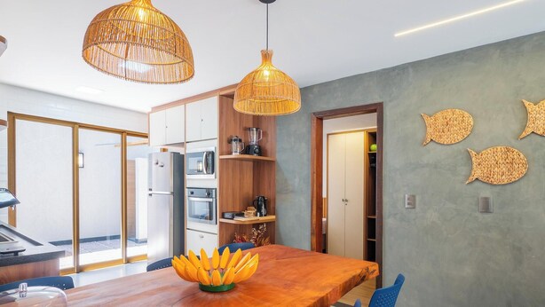A modern kitchen with wooden cabinets, a dining table, and a kitchen island. - Fully Equipped Aparts in Praia do Forte - PBS (Mata de São João)