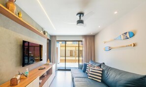 A modern living room with a flat-screen TV, a ceiling fan, a sofa with striped cushions, and two paddleboards on the wall.
