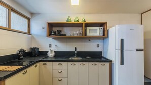 A compact kitchen with a refrigerator, microwave, and a shelf with glassware. - Fully Equipped Aparts in Praia do Forte - PBS (Mata de São João)