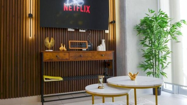 A modern living room with a flat-screen TV displaying the Netflix logo, a wooden entertainment unit, a round coffee table, a sofa, and a potted plant. - ¡Cerca de Fundidora! 6 personas, GYM & Wifi 2BR1br (Monterrey)