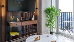 A modern living room with a large flat-screen TV mounted on a wooden wall, a round dining table with gold legs, and a balcony with a view of the city. - ¡Cerca de Fundidora! 6 personas, GYM & Wifi 2BR1br (Monterrey)