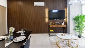 A modern living room with a wooden panel wall, a flat-screen TV, a dining table with chairs, and a small side table. - ¡Cerca de Fundidora! 6 personas, GYM & Wifi 2BR1br (Monterrey)