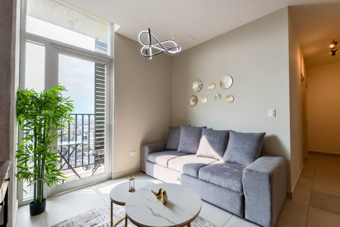 A modern living room with a grey sofa, a small round table, and a potted plant by the window.