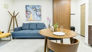 A modern living room with a blue sofa, a wooden dining table with chairs, a painting on the wall, and a vertical wooden panel. - ¡Cerca de Fundidora! 6 ppl, GYM, Parking & 3 camas (Monterrey)
