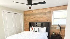 Camera da letto con un letto, pareti in legno, una ventola a soffitto, un comodino e una finestra.