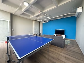 Una habitación con mesa de ping pong, sofá, televisor y una pared azul de acento.