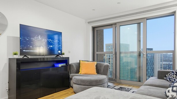 A modern living room with a flat-screen TV, grey sofas, and a large window with a city view. - Entire City View Apartment 8 mins to London Brigde (London)
