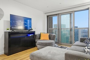 Un salon moderne doté d’un téléviseur à écran plat, de canapés gris et d’une grande fenêtre offrant une vue sur la ville.