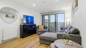 A modern living room with a flat-screen TV, grey sofas, a round coffee table, and a large window with a city view. - Entire City View Apartment 8 mins to London Brigde (London)