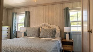 Une chambre à coucher comprenant un lit, des tables de chevet, une commode et une fenêtre avec des rideaux.